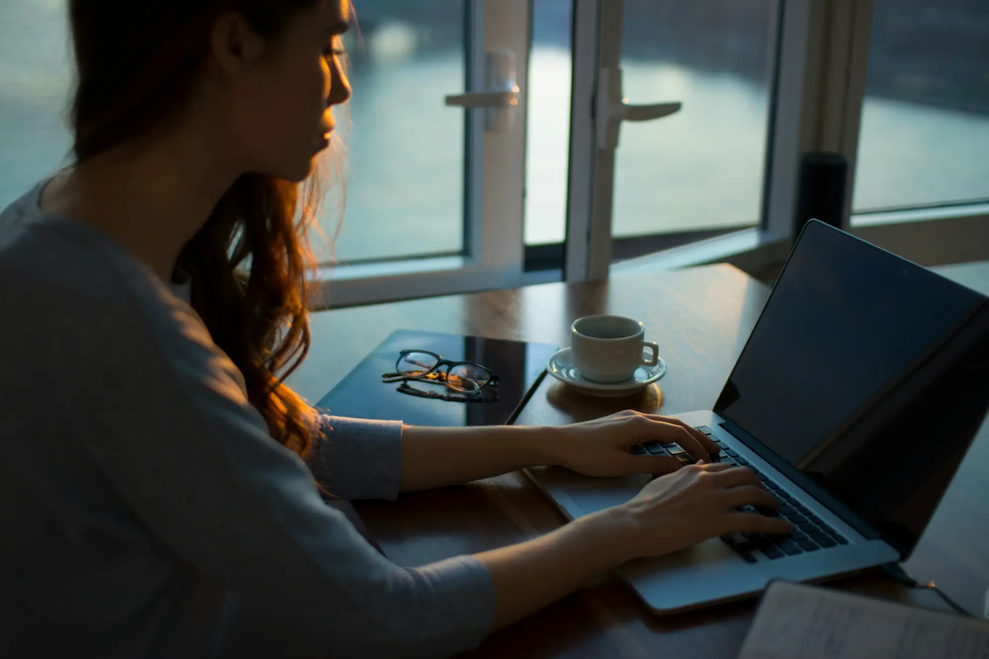 A woman working through papers at a laptop by a window